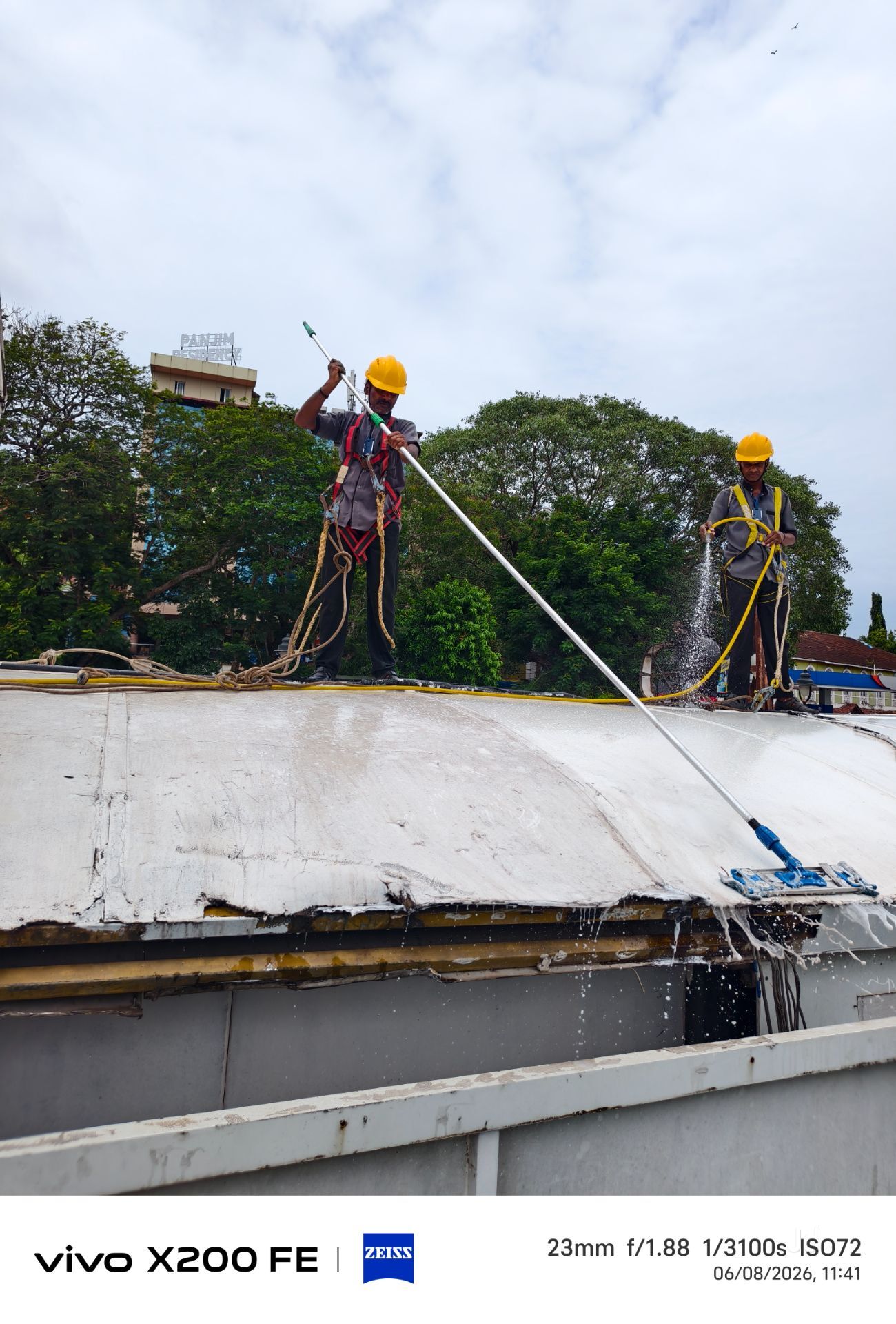 Two harnessed workers pressure washing a curved roof structure